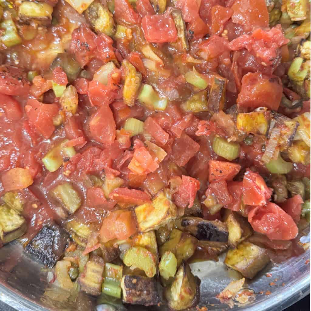 Tomatoes stirred into the pan, sauce thickening for Sicilian caponata.