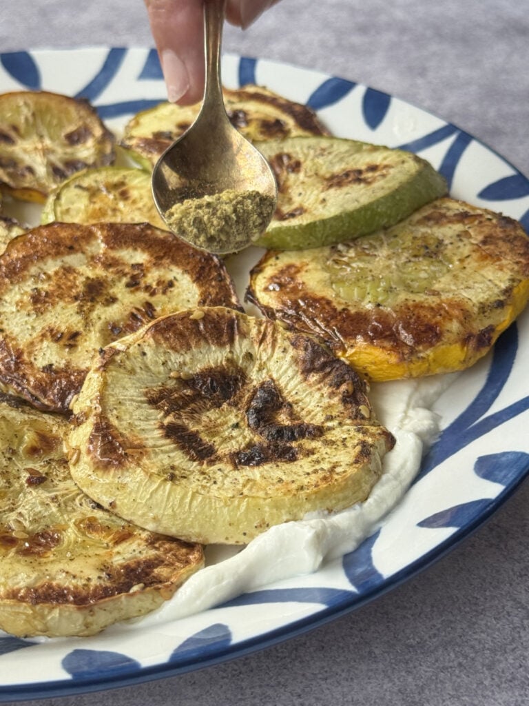 Broiled zucchini plated over swirled lebneh, finished with herbs and a dusting of za'atar.