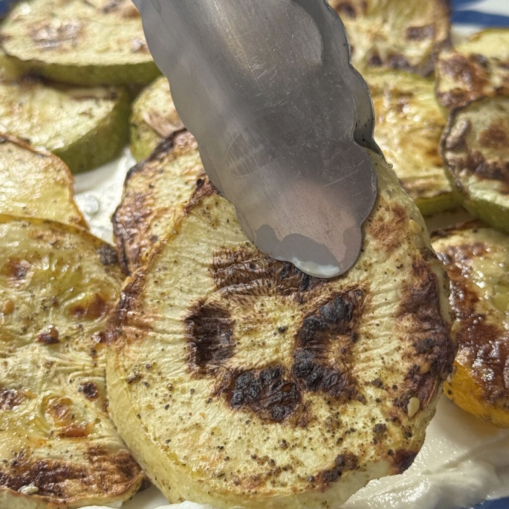 Zucchini served tableside with tongs over a platter of lebneh.