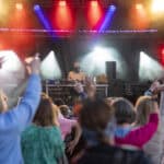 Crowd enjoying live music at outdoor festival with colourful stage lights.