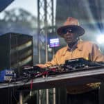 DJ wearing sunglasses and hat performing at outdoor music festival.