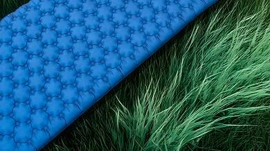 Lightweight camping sleeping mat with pillow and backpack on grassy outdoor terrain.