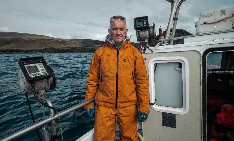 1. Man in orange offshore waterproof jacket on boat during sea expedition.