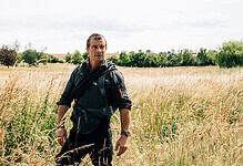 Wildlife enthusiast walking through a field of tall grass in a scenic countryside landscape.