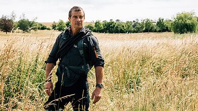 Wildlife enthusiast walking through a field of tall grass in a scenic countryside landscape.