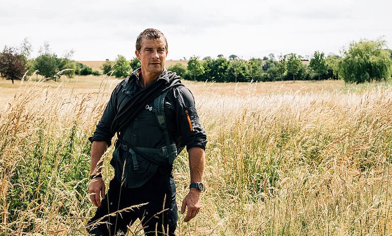 Wildlife enthusiast walking through a field of tall grass in a scenic countryside landscape.