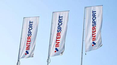 Three Intersport flags flying in the wind at an outdoor sports event.