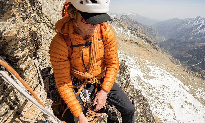 Climber in orange jacket ascending mountain with safety gear.