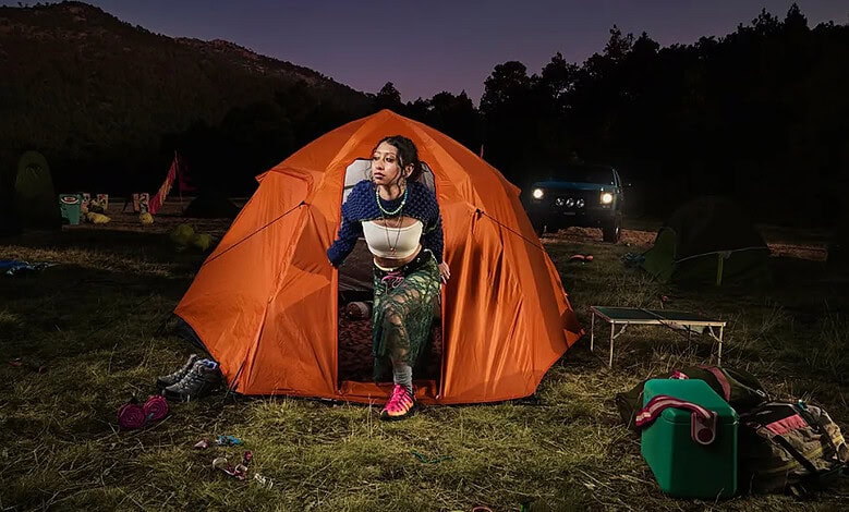 Woman sitting outside an orange tent during night camping.