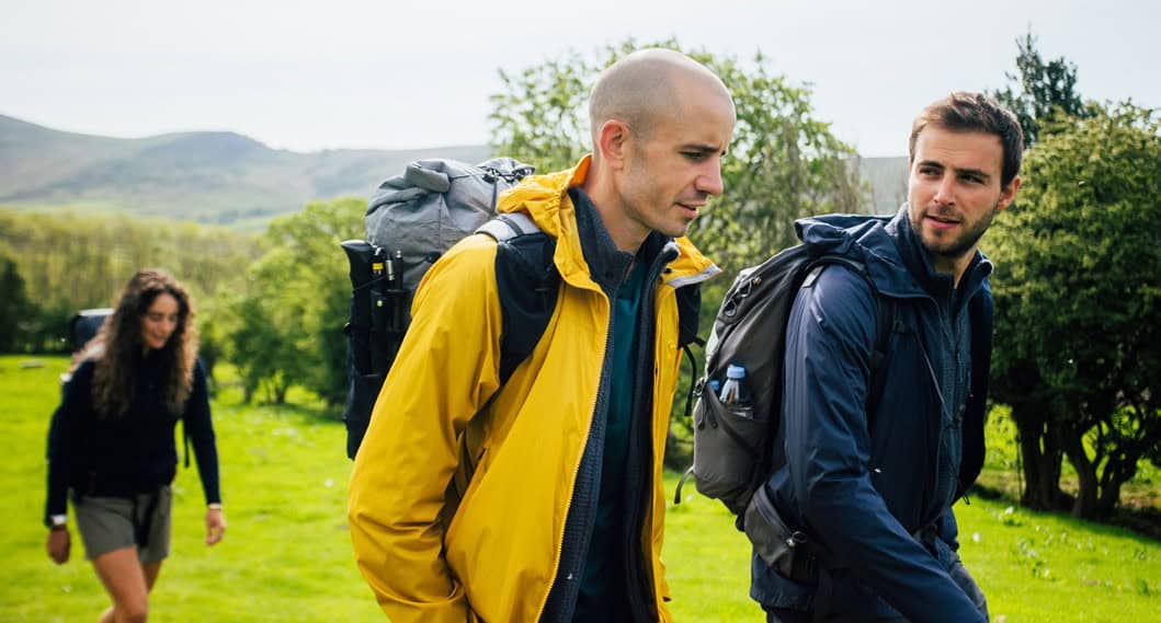 Hikers walking through lush green landscape with backpacks, enjoying outdoor adventure.