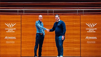 Two men shaking hands at Glasgow 2026 event with RIEDEL branding.