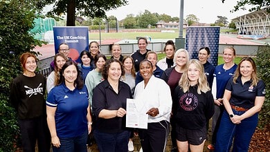 Group of women at UK Coaching Summit with outdoor sports facilities in background.