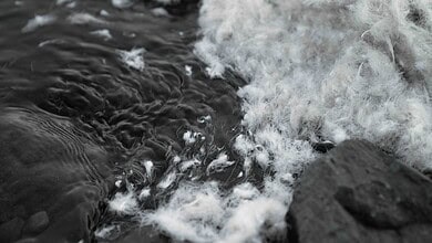 Close-up of water flowing over rocks with foam and bubbles.