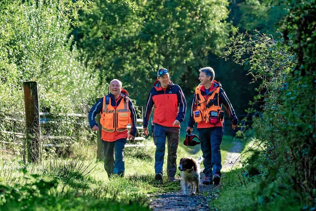 Outdoor group walking with search dog at Bewl Water in lush greenery.