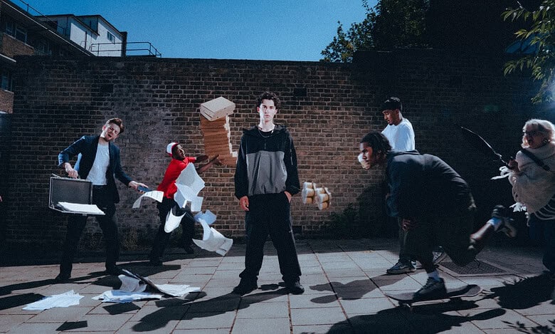 Young men in streetwear amidst flying papers and debris outdoors.