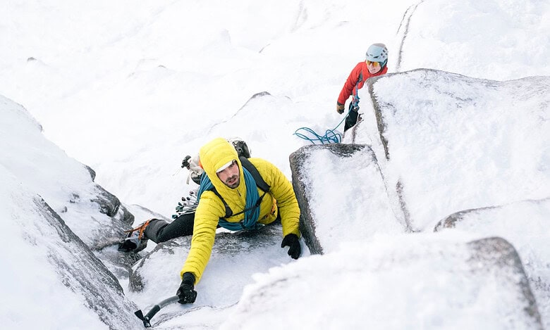 Climber ascending icy rock face with safety gear in snowy mountain terrain.