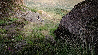 Scenic landscape with large rocks, green hills, and a person sitting on a boulder.