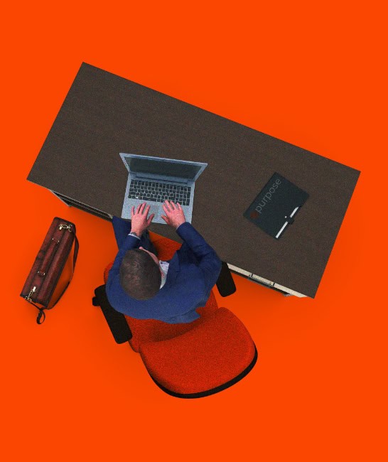 Purpose Solutions Managed Services A man sitting at a desk on his computer with a Purpose logo folder.