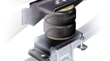 A close-up view shows a black, cylindrical Firestone air spring suspension component installed on a vehicle's suspension system.