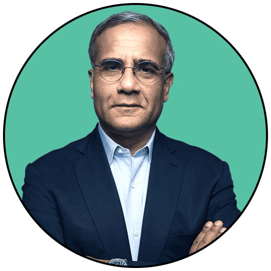 Senior businessman in a navy suit with crossed arms against a teal background.
