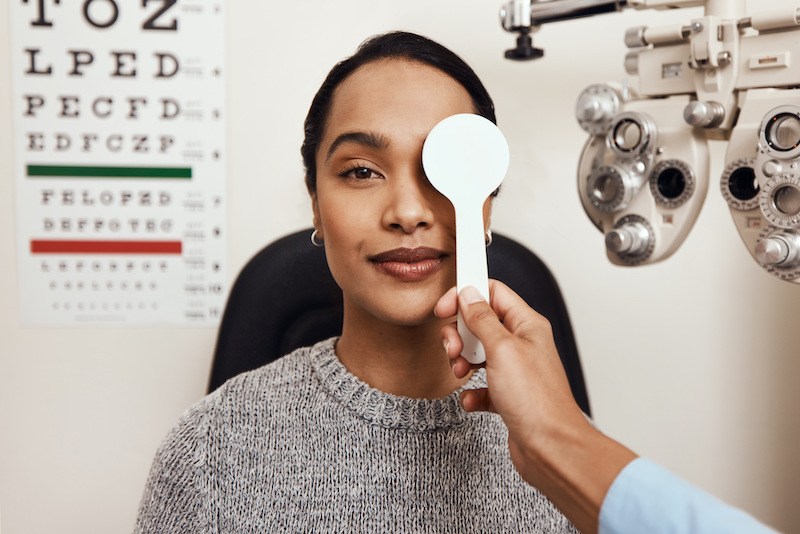 Optometrist performing eye health check with phoropter and eye chart in background.