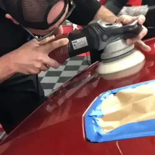 Technician performing paint correction on red car