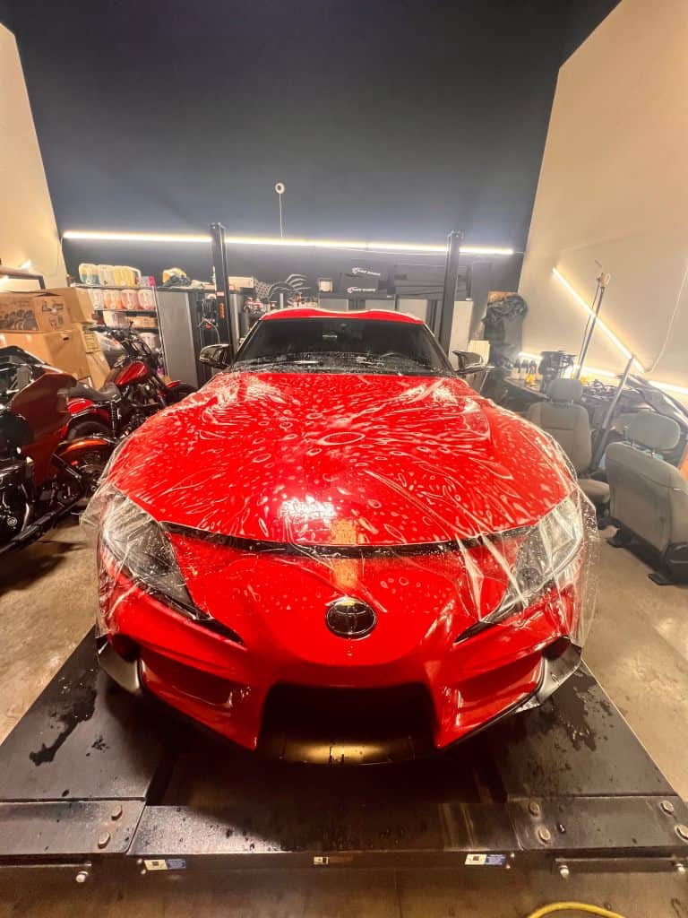 Red sports car covered in water droplets at T1Detailing workshop.