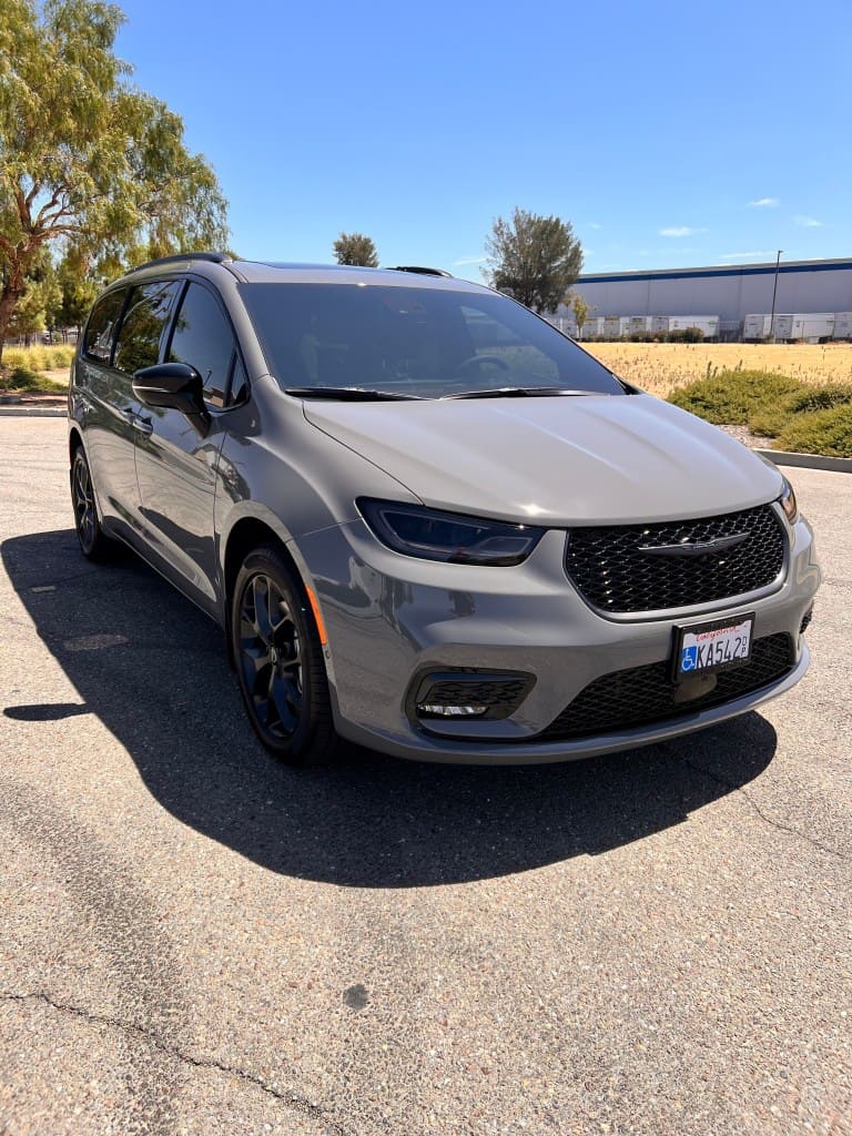 Gray minivan parked outdoors with trees and blue sky in background.