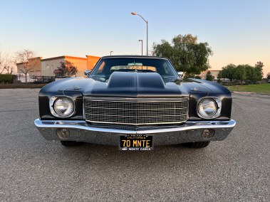 Vintage black muscle car with custom grille and California license plate.