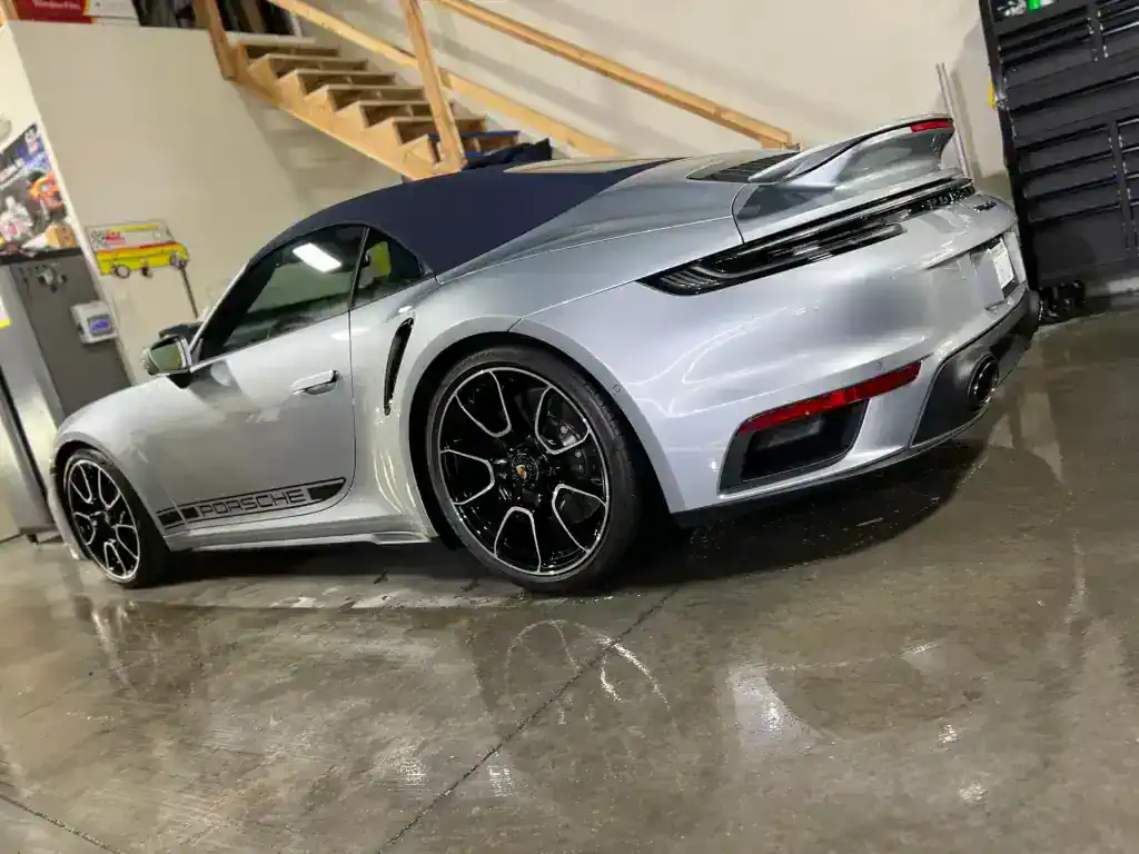 High-end silver Porsche sports car in detailing shop with black wheels.