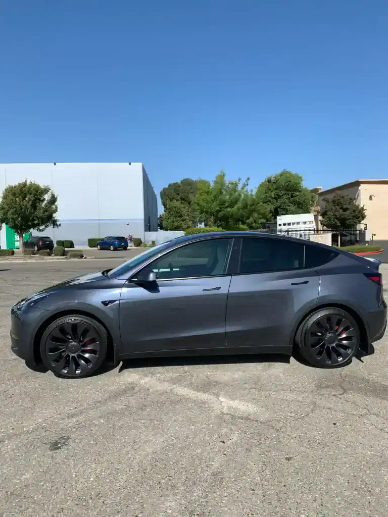 Sleek gray luxury car with black rims parked outdoors under clear blue sky.