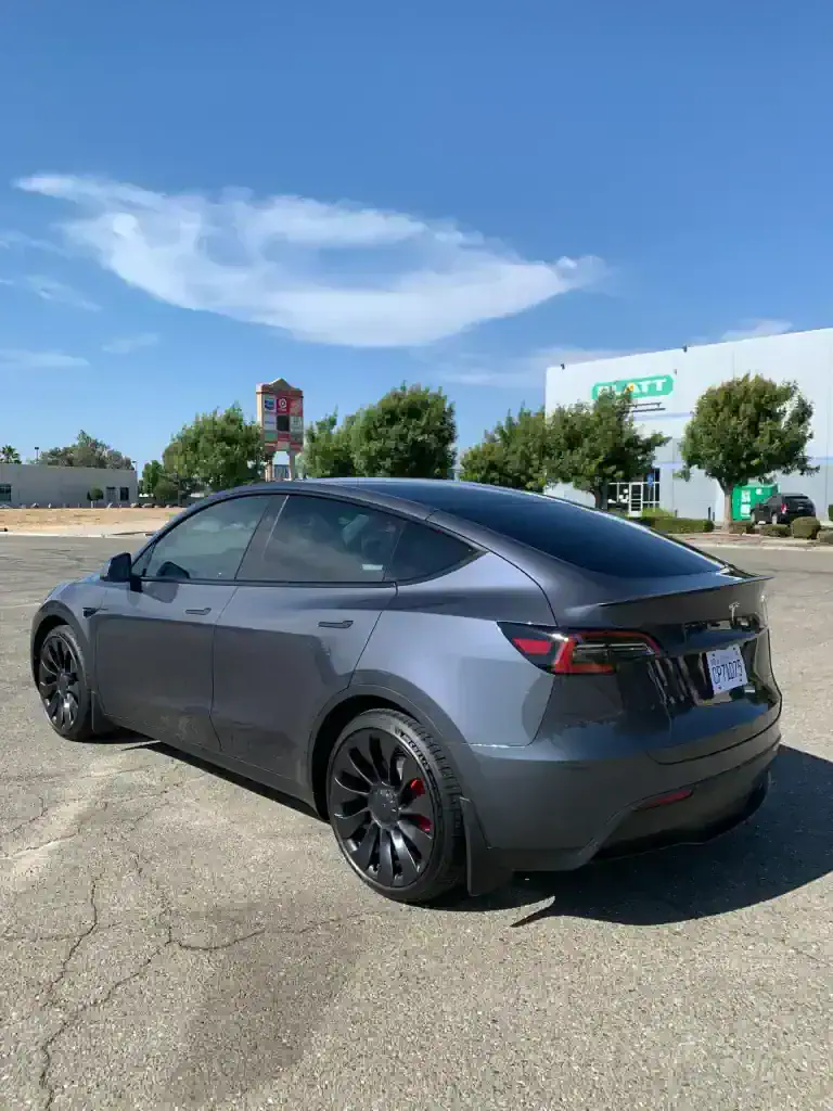 Tesla Model Y parked outdoors with clear blue sky and trees in background.