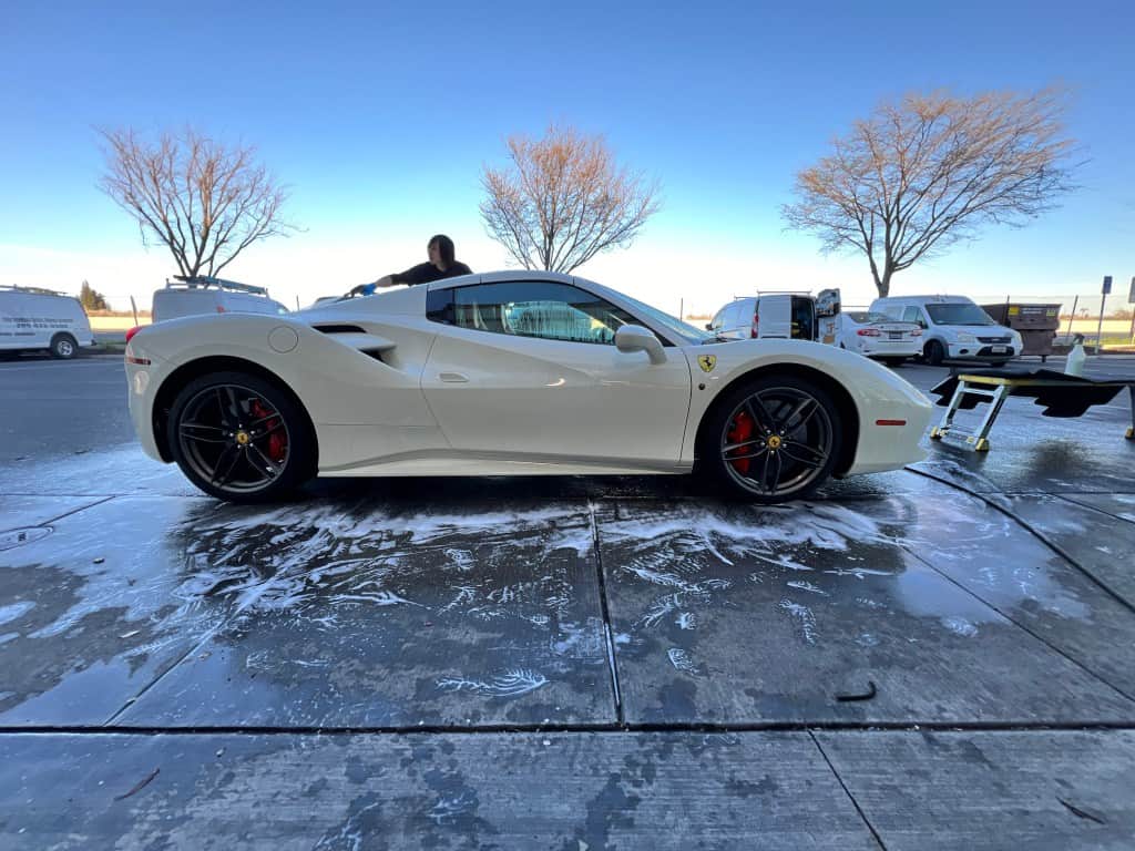 White sports car being detailed outdoors with cleaning equipment.