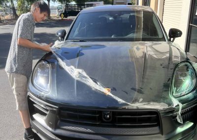 Person detailing a black sports car outdoors on a sunny day.