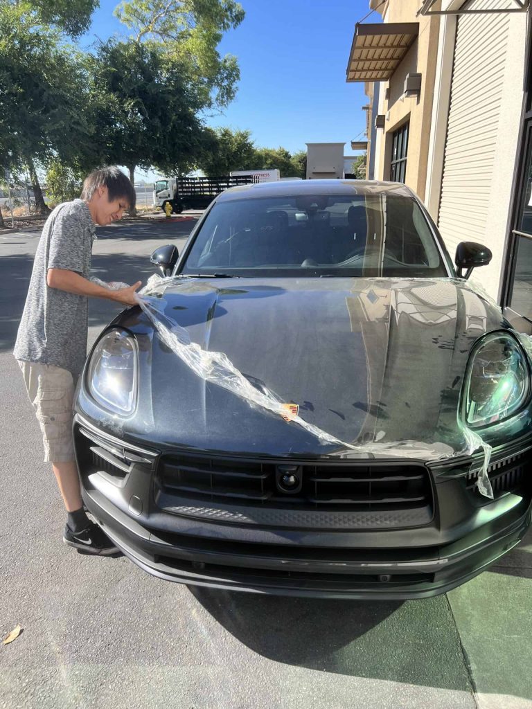 Person detailing a black sports car outdoors on a sunny day.