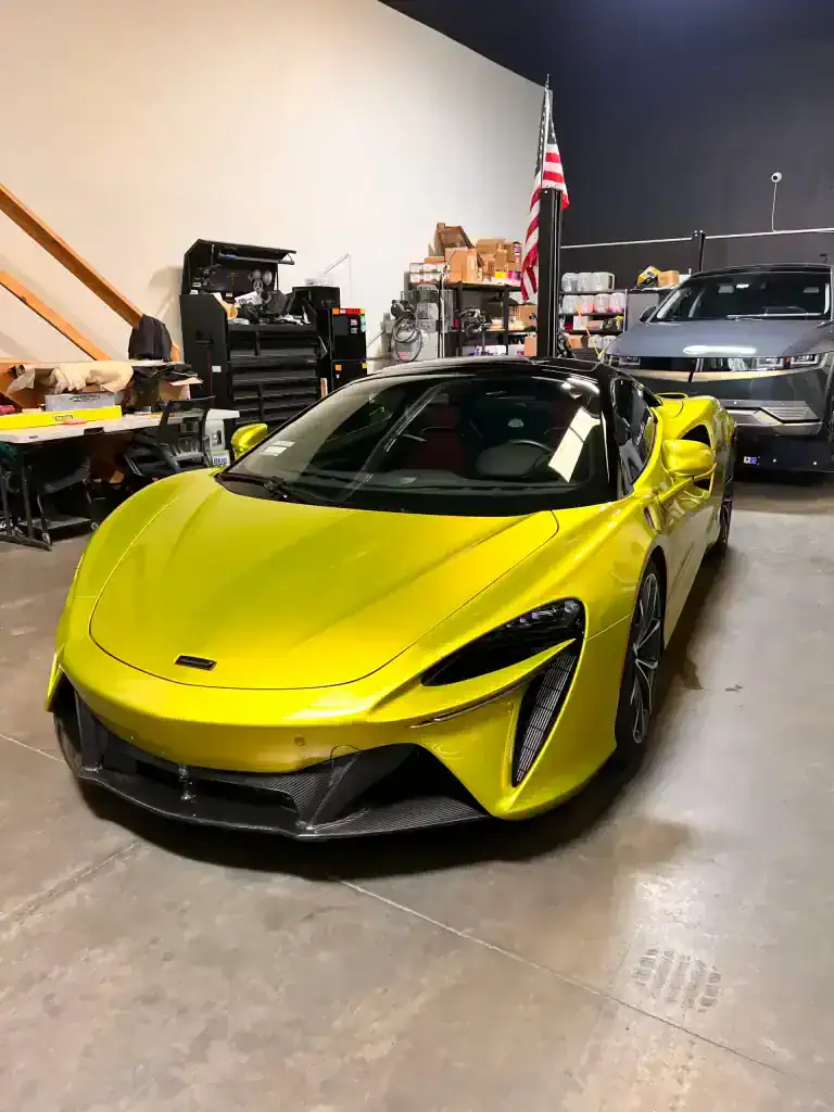 Yellow McLaren sports car inside detailing shop with tools and equipment.