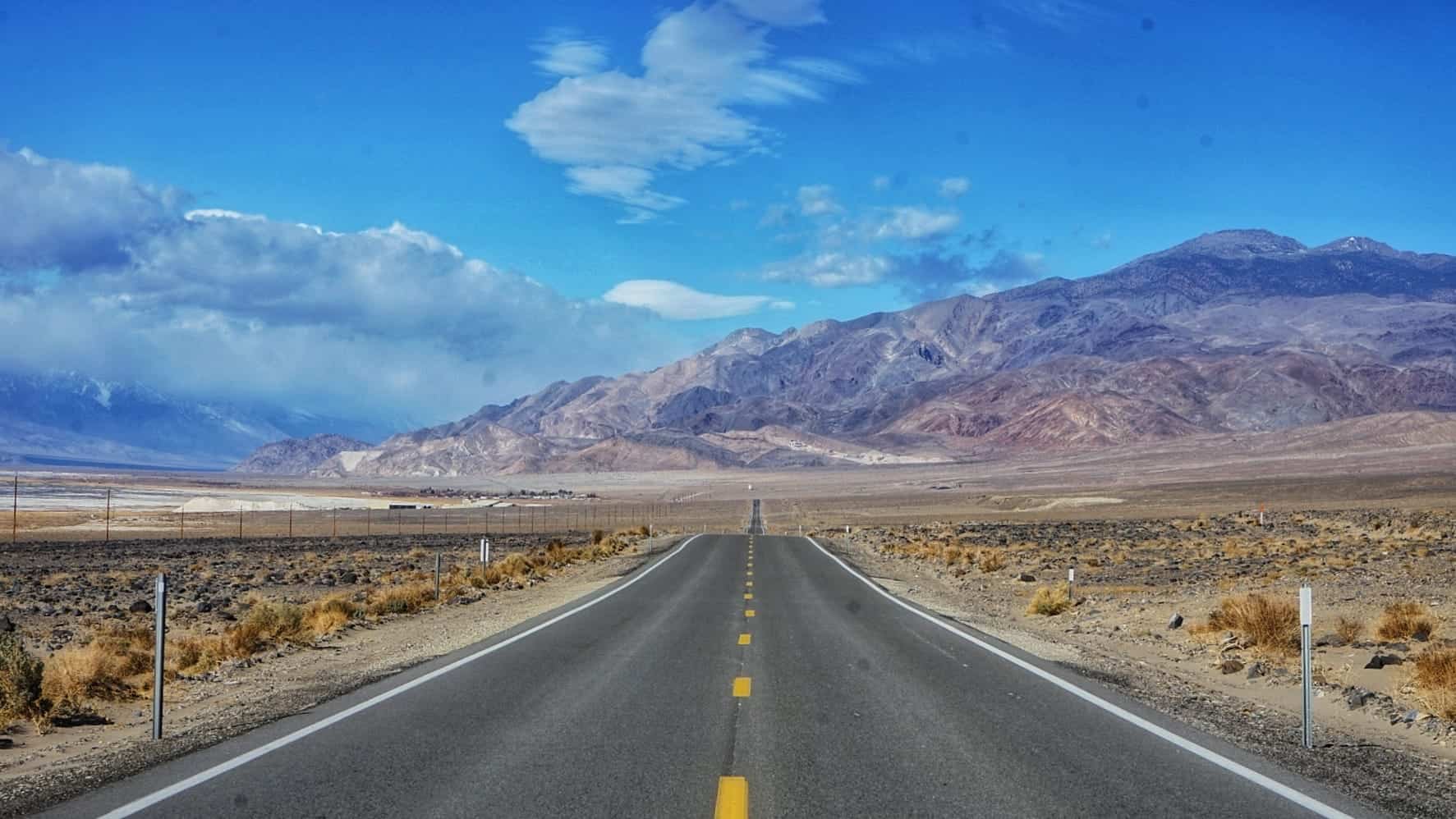 Strada deserta nel deserto con montagne e cielo azzurro.