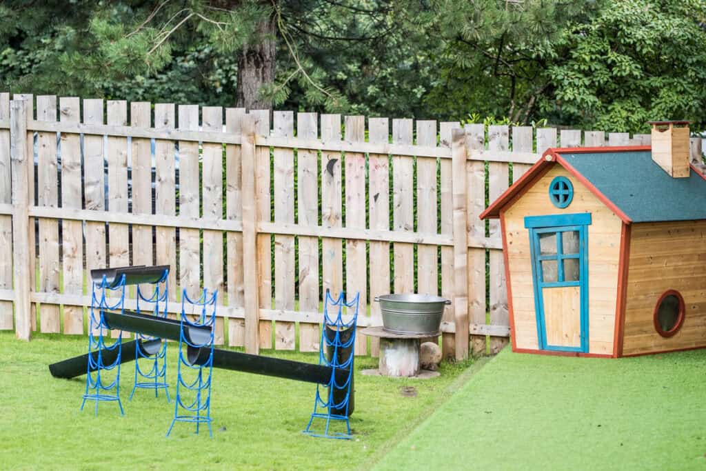 Bright outdoor play area at Thrive Childcare featuring a wooden playhouse, climbing equipment, and a grassy yard for children's fun and development.
