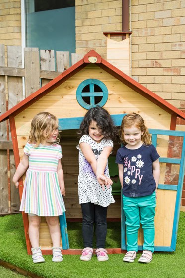 Colourful outdoor playhouse with three smiling children in a childcare setting, promoting fun, learning, and social development at Thrive Childcare.