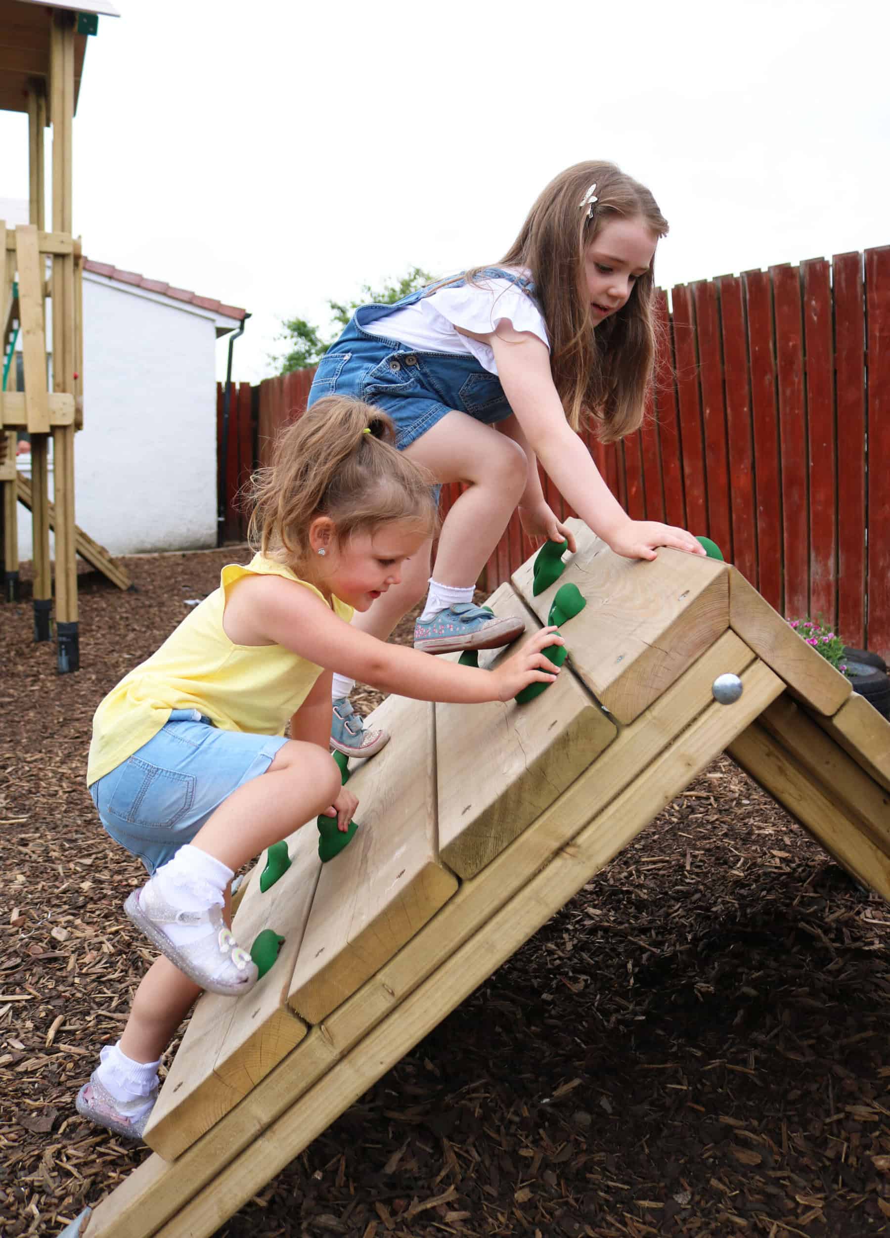 Brightly coloured children climbing on an outdoor wooden play structure at Thrive Childcare, encouraging active play and physical development.