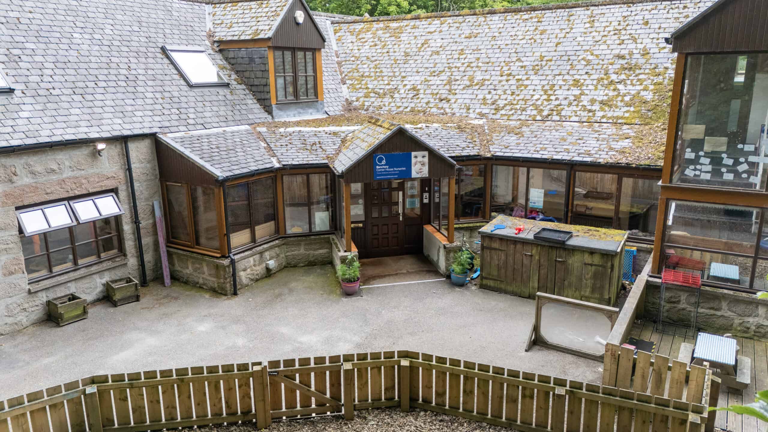 Bright and welcoming childcare centre with outdoor play area at Thrive Childcare, featuring a courtyard, garden space, and cosy building with large windows for a nurturing early education environment.