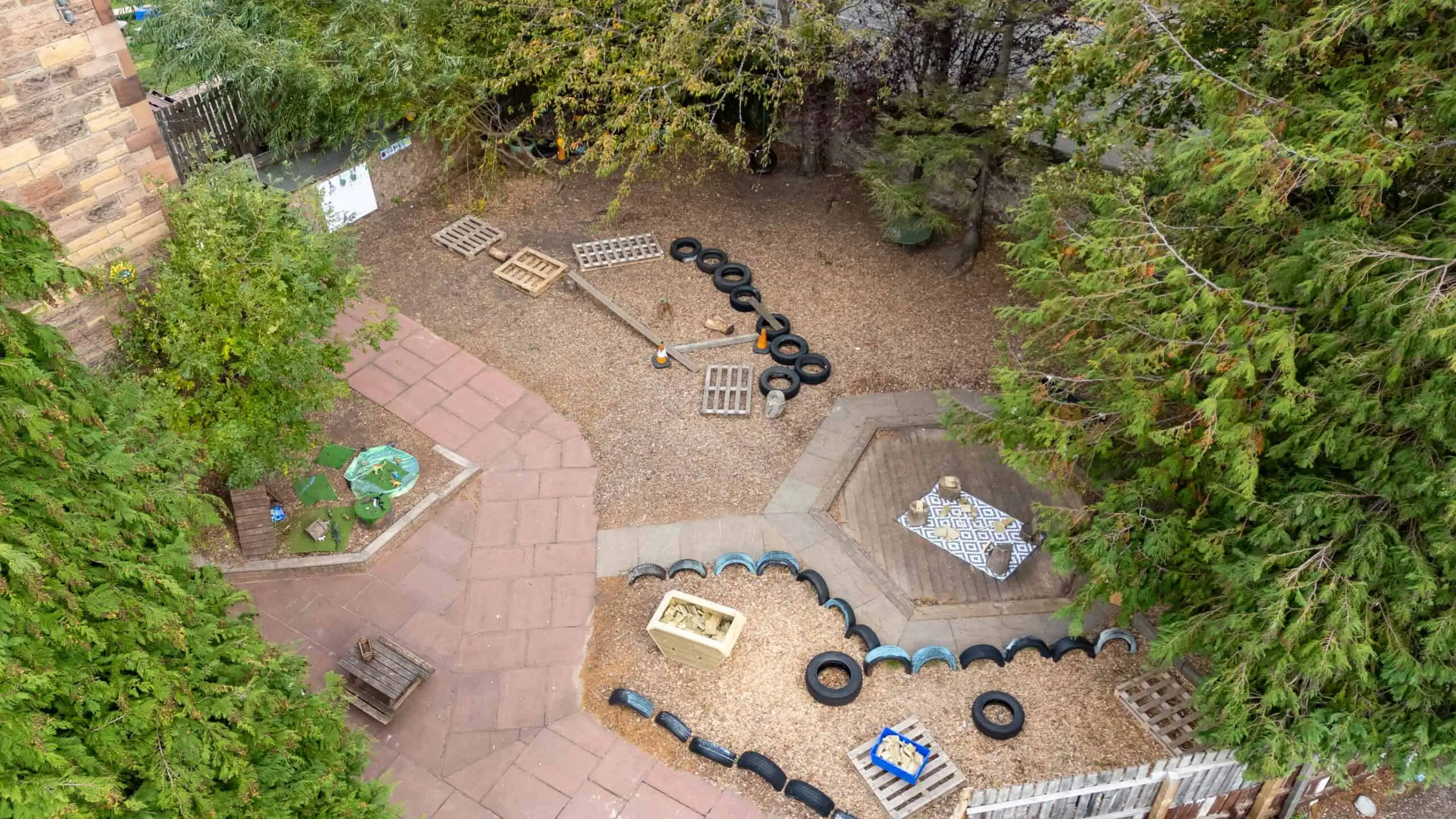 Bright children's outdoor play area with tire obstacle course, wooden pallets, sandpit, and seating area, ideal for early childhood development, outdoor activities, and imaginative play.