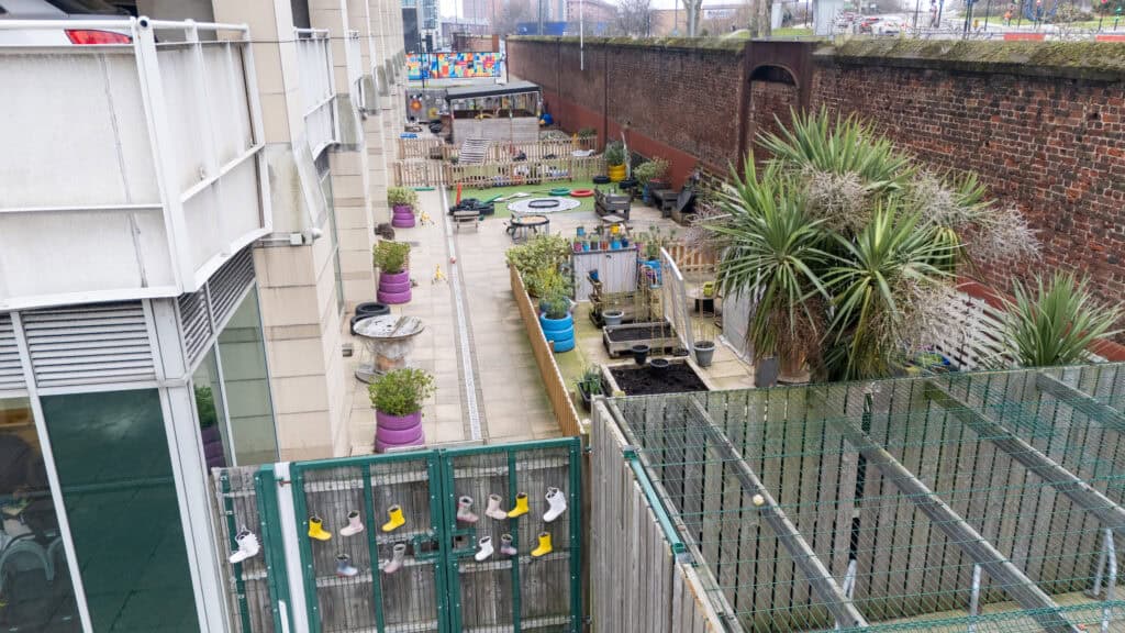 Outdoor play space at Thrive Childcare Holyrood Nursery Princes Dock with vibrant toys, lush greenery, and secure fencing, providing a safe environment for children's outdoor activities and learning.