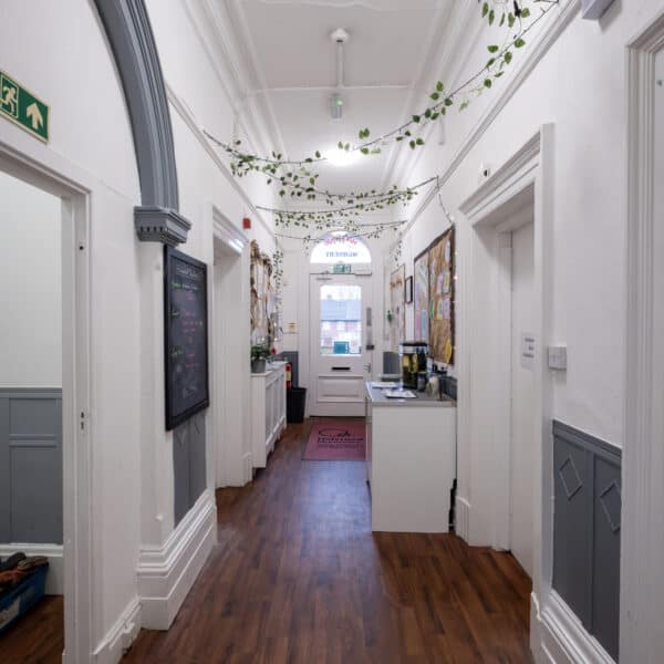 Indoor corridor of Thrive Childcare with white walls, wooden flooring, and decorative foliage on the ceiling, creating a welcoming environment for children and families.