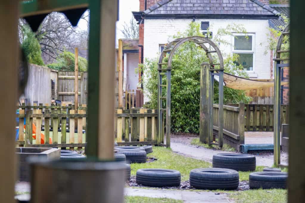 Bright outdoor play area at Thrive Childcare featuring a wooden climbing frame, garden, and safety tires, providing a safe and engaging environment for children's outdoor development and fun.
