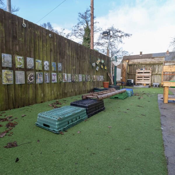 Bright outdoor childcare play area at Thrive Childcare, featuring colourful educational wall art, step platforms, and secure fencing, designed for early childhood development and safe fun.