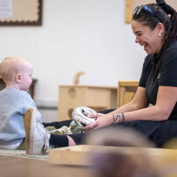 Brightly smiling nursery staff engaging with happy toddler during playtime at Thrive Childcare in a welcoming early years education environment.