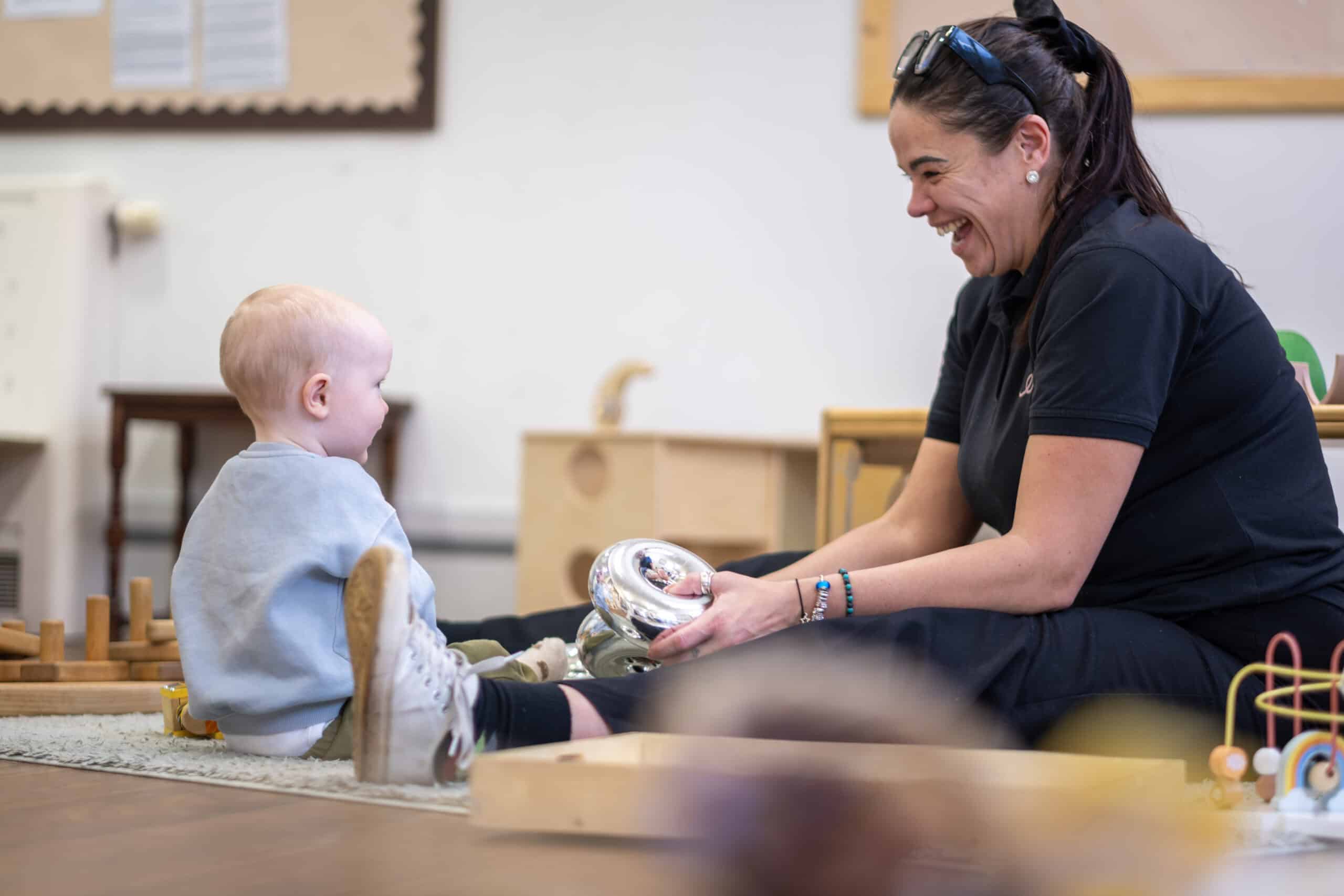 Brightly smiling nursery staff engaging with happy toddler during playtime at Thrive Childcare in a welcoming early years education environment.