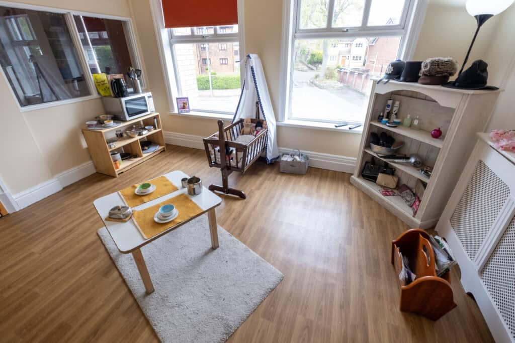 1. Bright childcare room with wooden flooring, baby crib, toys, and soft furnishings at Thrive Childcare, creating a welcoming environment for children's early development.
