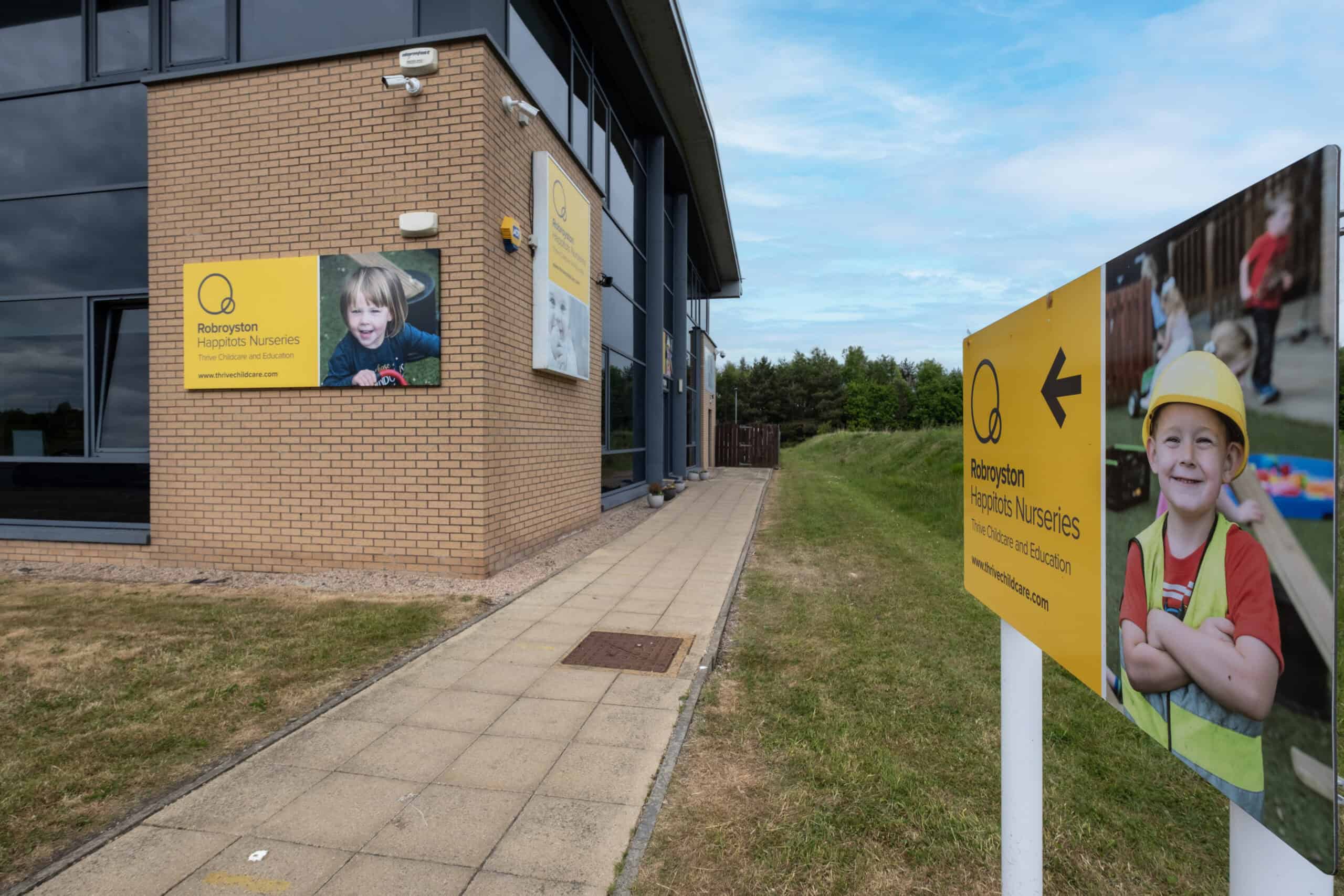 Bright outdoor signage for Thrive Childcare and Nurseries in Robroyston, featuring happy children and colourful images promoting early childhood education and nursery services.